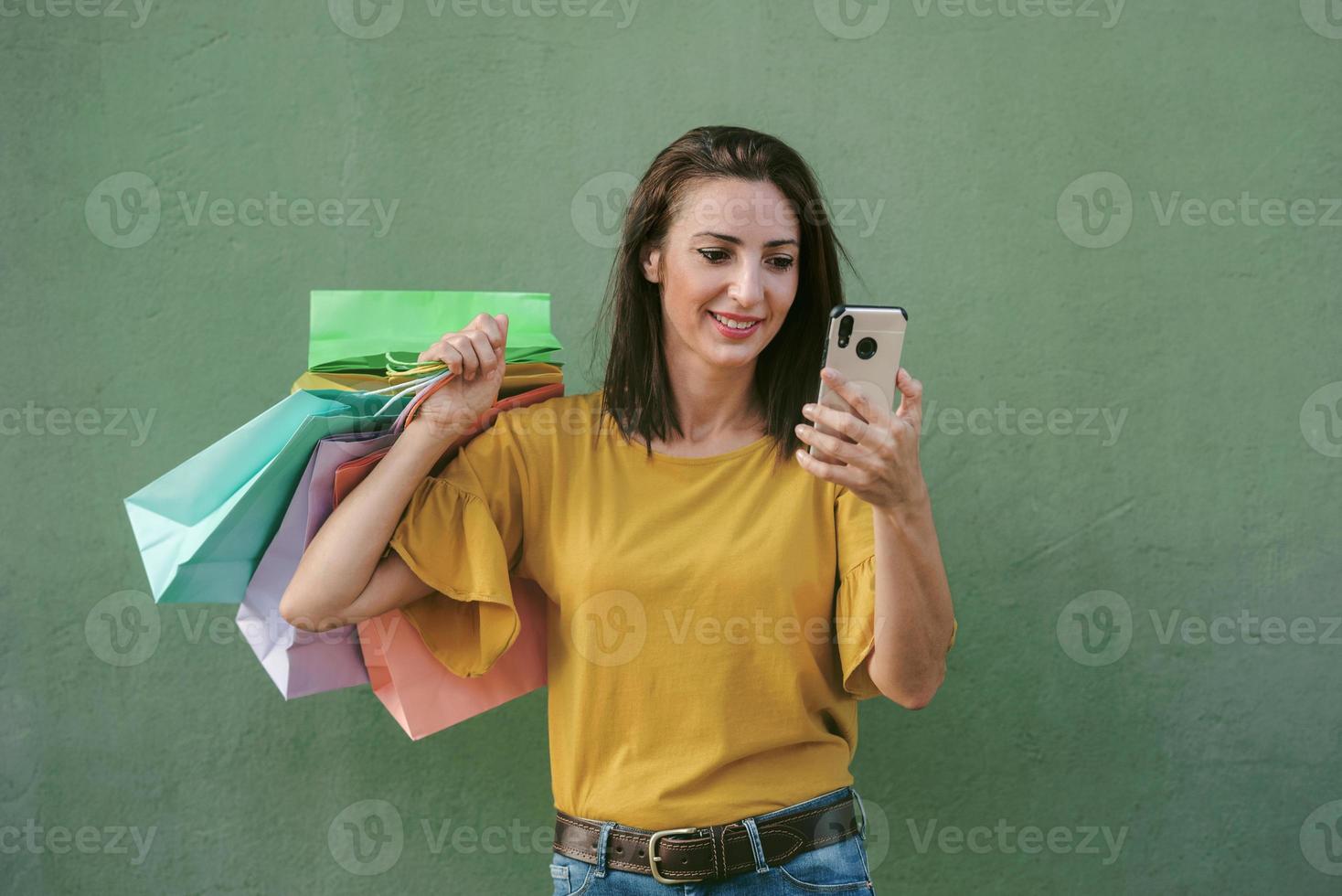 jovem mulher feliz segurando um smartphone e sacolas de compras foto