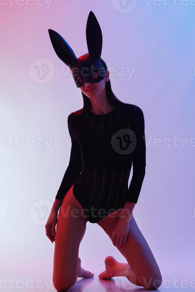 mulher sexy vestindo uma máscara preta coelhinho da páscoa em pé sobre um fundo azul e parece muito sensual foto