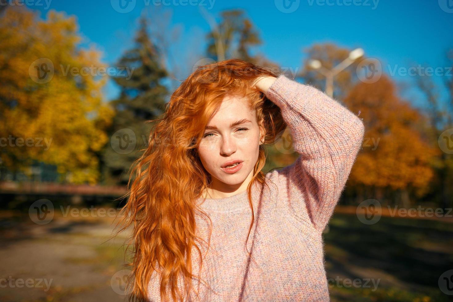 retratos de uma encantadora garota ruiva com um rosto bonito. garota posando no parque outono em um suéter e uma saia cor de coral. a menina tem um humor maravilhoso foto