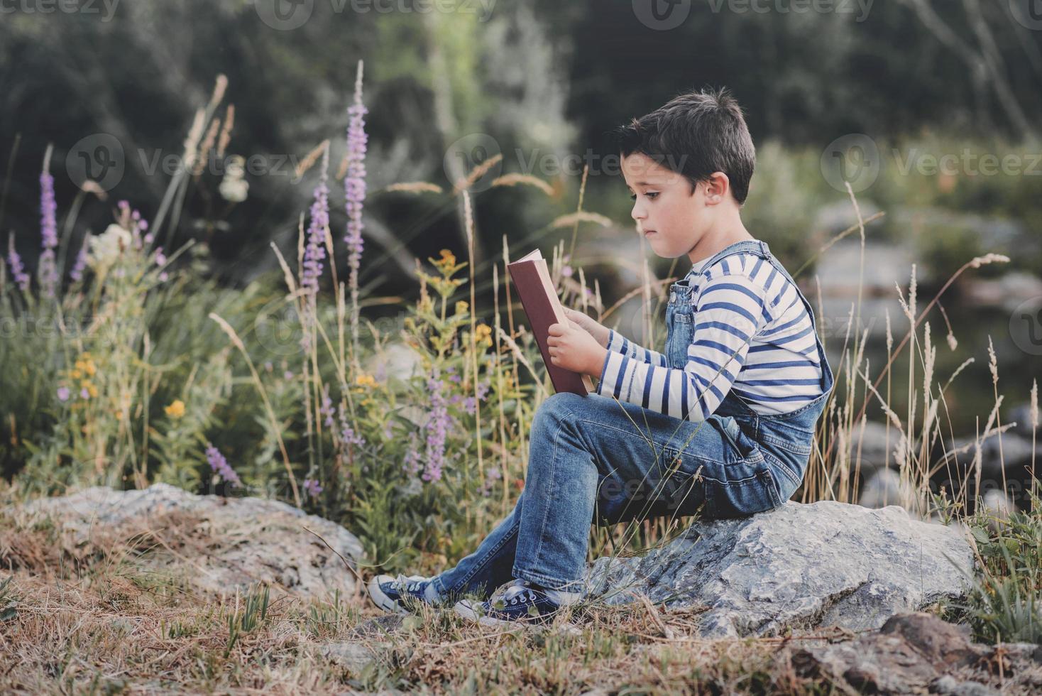 criança sentada lendo um livro no campo foto