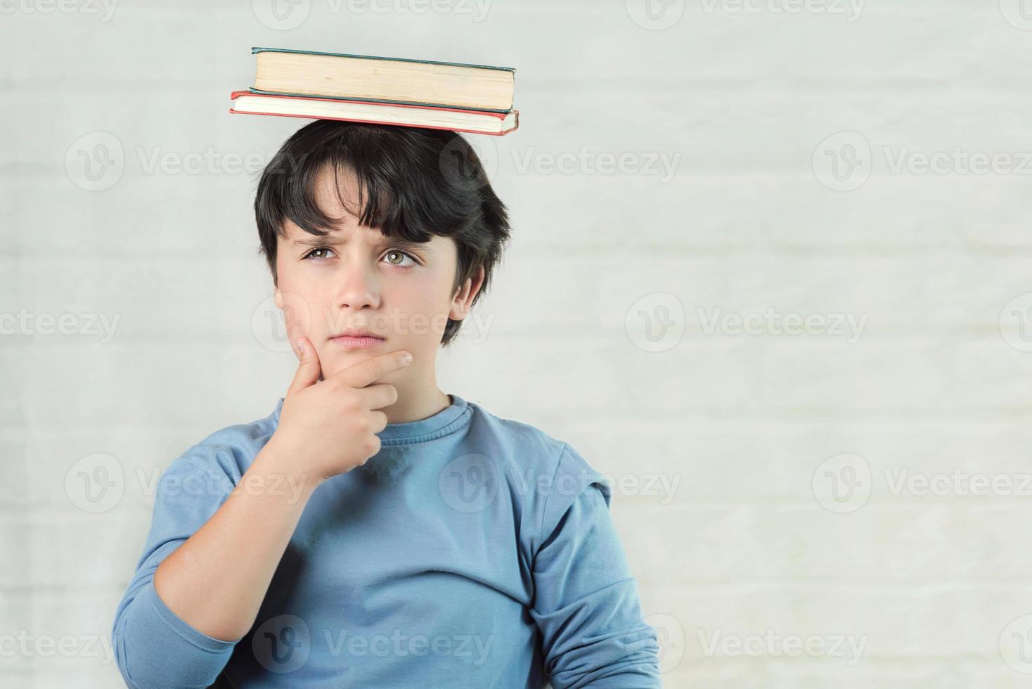 criança pensativa com livros na cabeça foto