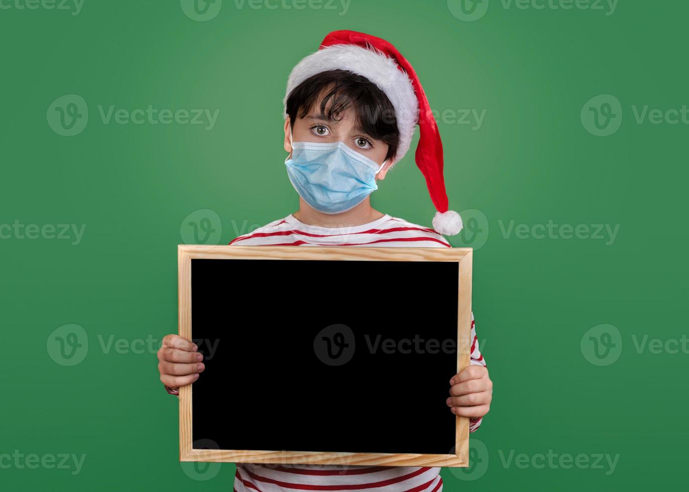 feliz natal, garoto engraçado com máscara médica segurando um quadro-negro foto