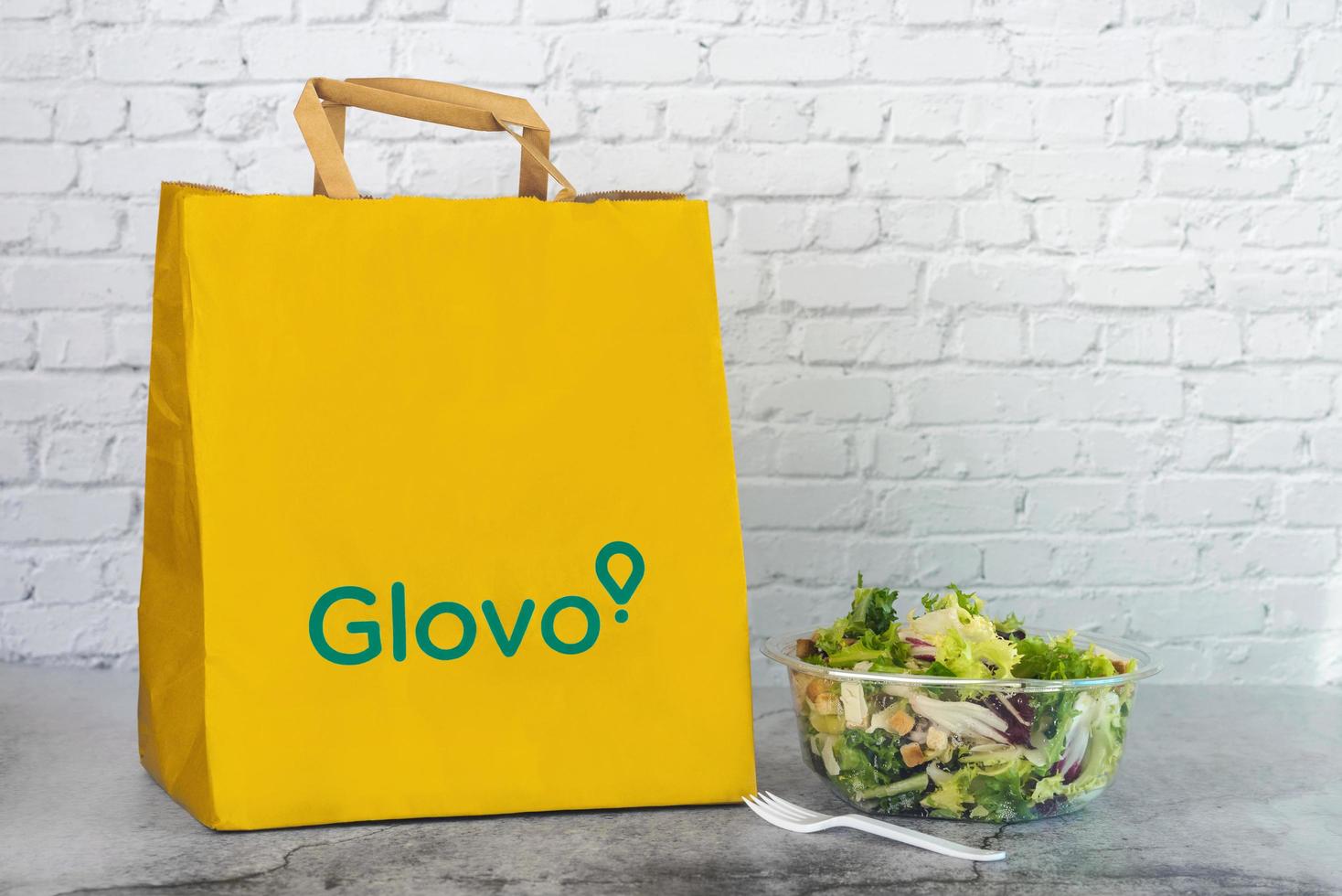 saco de entrega de papel de comida glovo ao lado de uma salada foto