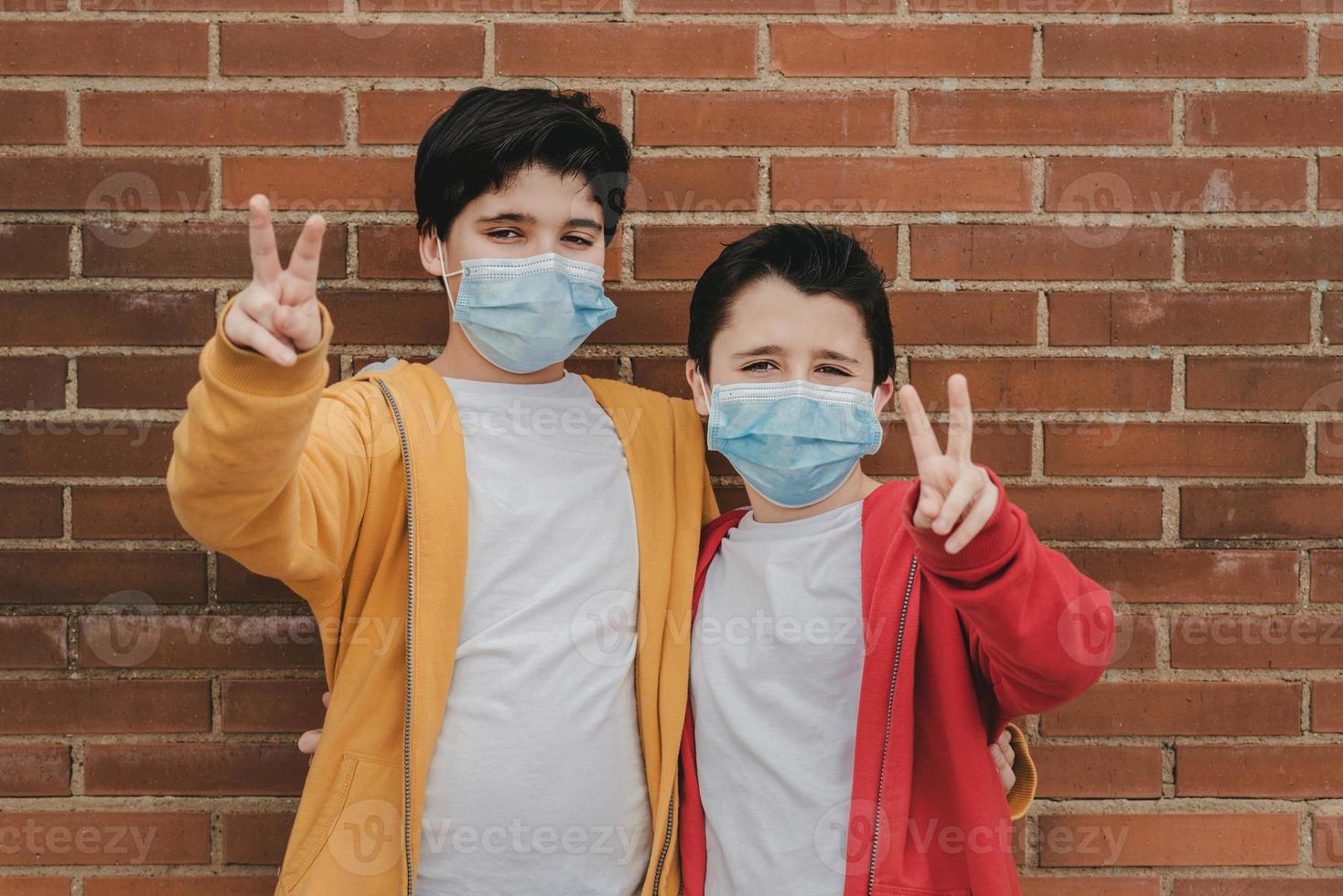 duas crianças com máscara médica fazendo sinal de vitória foto