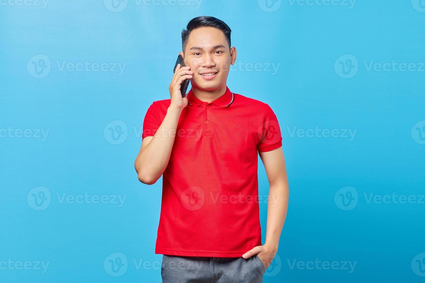 retrato de homem asiático atraente falando no smartphone e parecendo feliz isolado em fundo azul foto