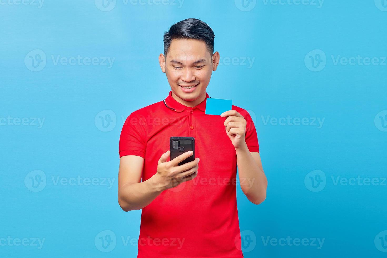 retrato de jovem asiático sorridente usando telefone celular e mostrando fundo azul isolado de cartão de crédito foto