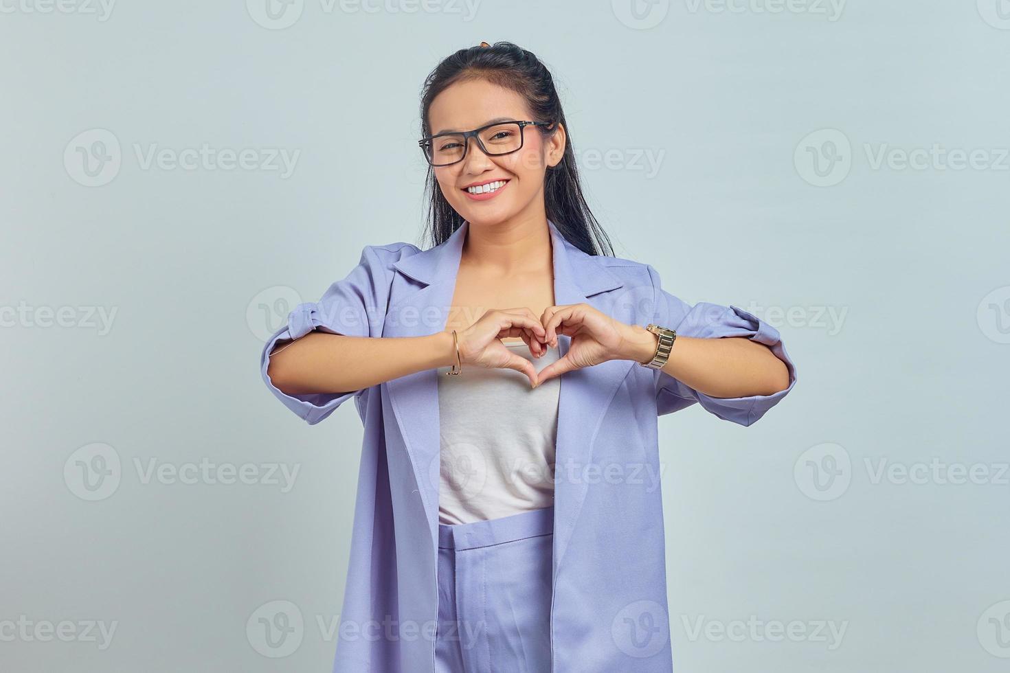 retrato de uma jovem asiática sorridente, mostrando o gesto do coração com as duas mãos e olhando para a câmera isolada no fundo branco foto