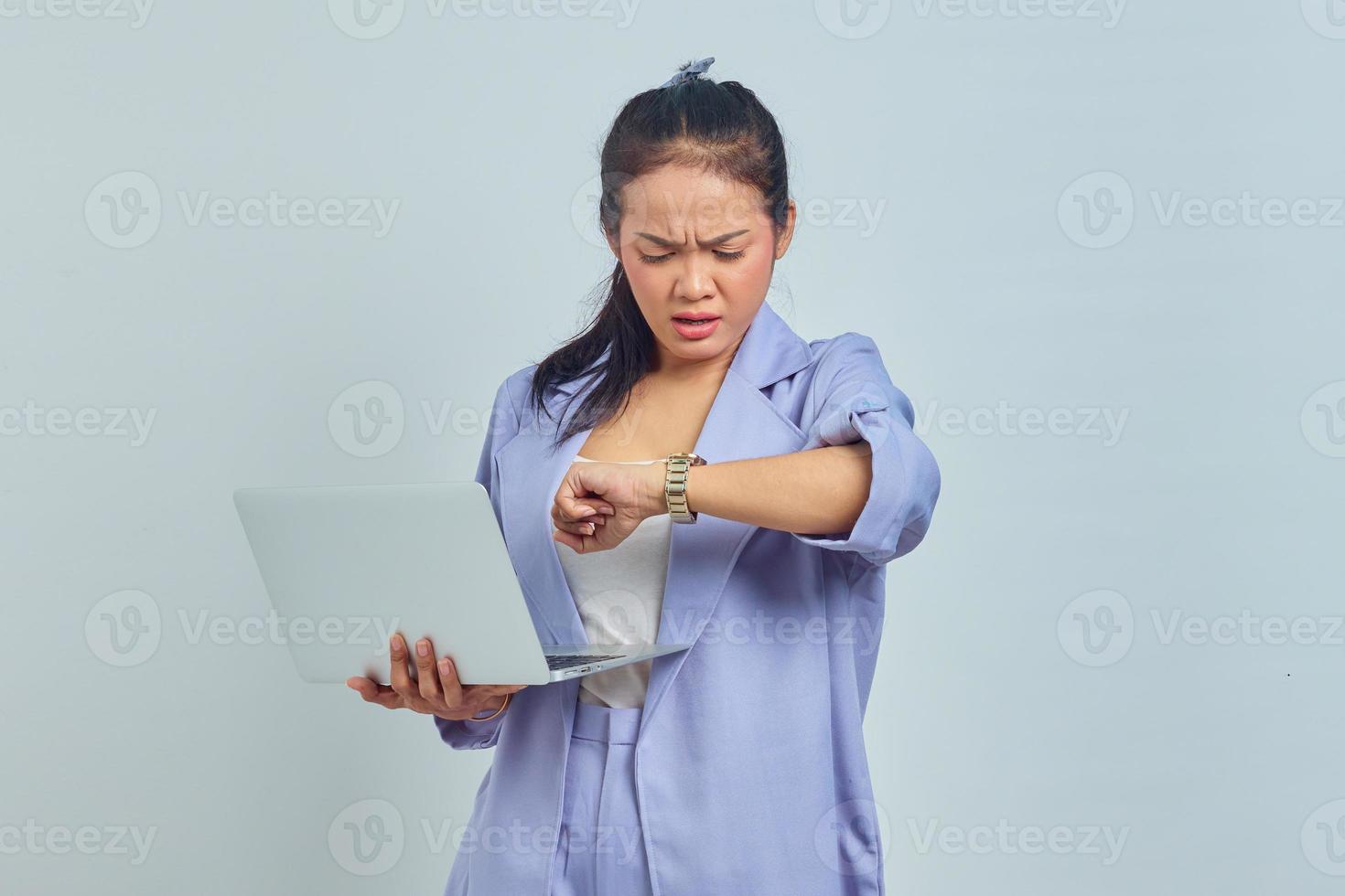 retrato de uma jovem asiática surpresa usando laptop e verificando o tempo no relógio isolado no fundo branco foto
