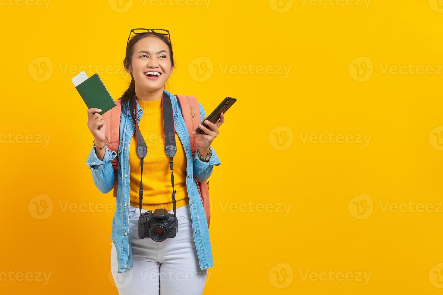 retrato de alegre jovem viajante asiático segurando o bilhete de embarque do passaporte e smartphone isolado em fundo amarelo. passageiros que viajam nos fins de semana. conceito de viagens aéreas foto