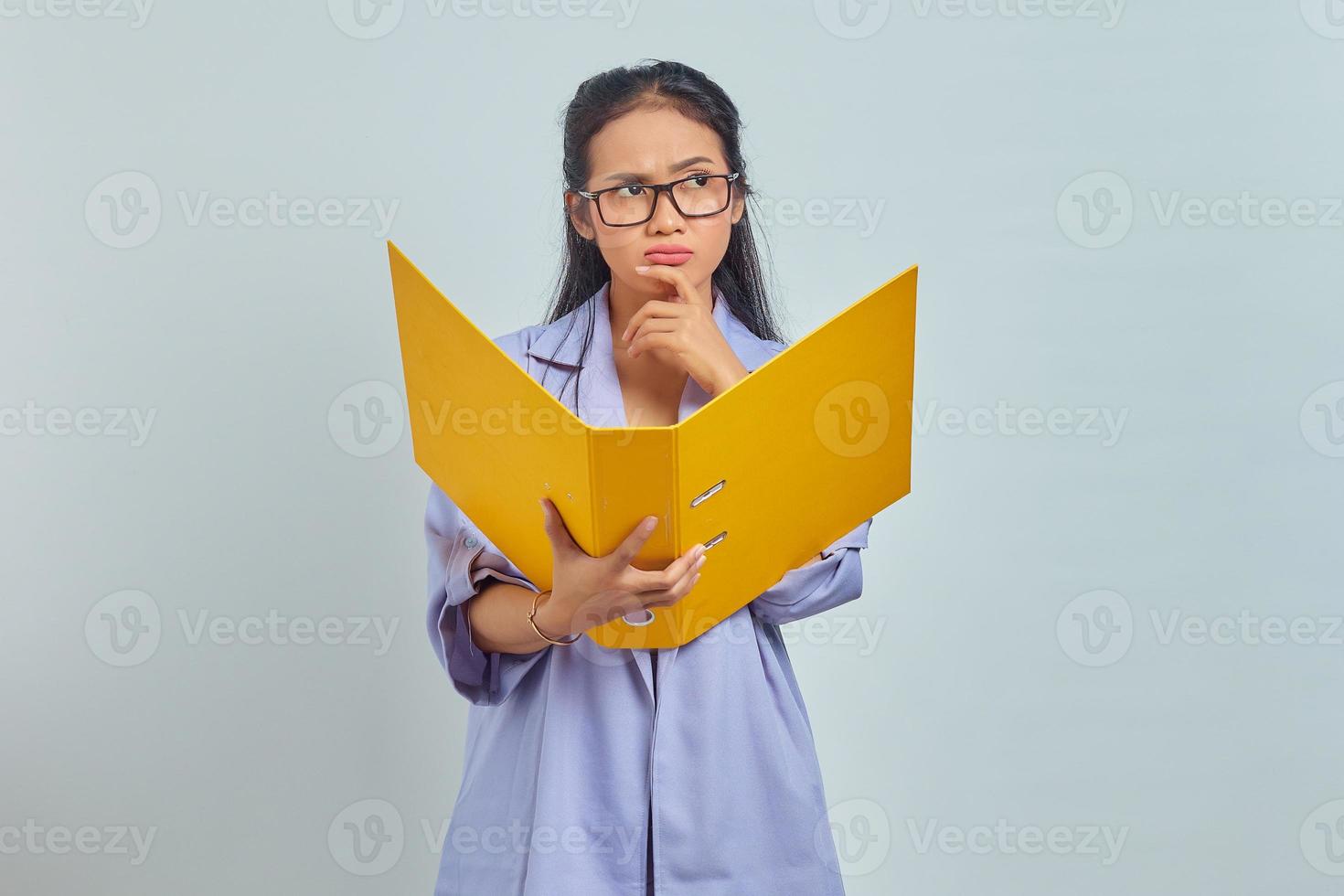 retrato de uma jovem empresária asiática séria segurando o queixo, contemplando algo enquanto segura a pasta de documentos isolada no fundo roxo foto