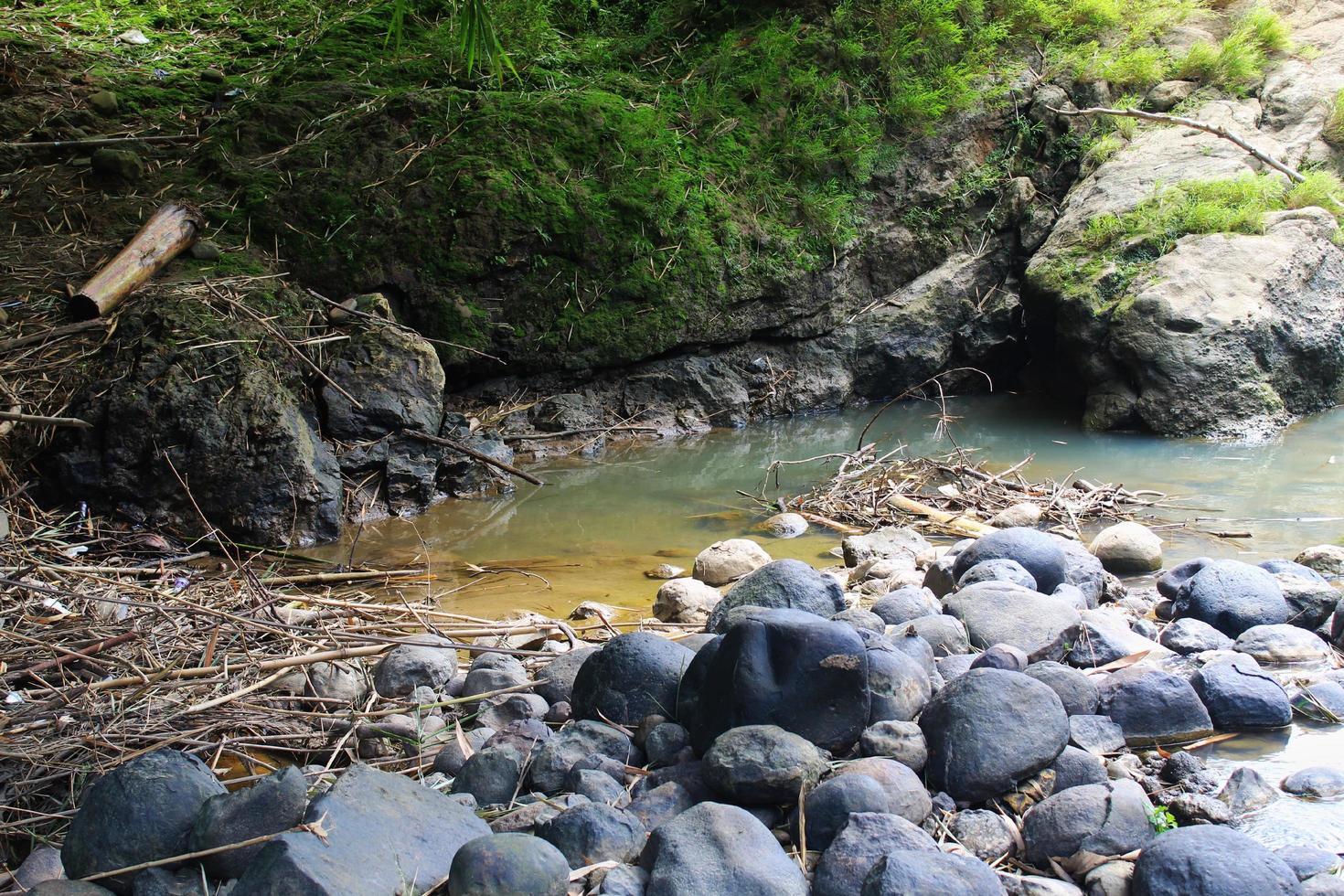 muitas pedras pretas, pedras cobertas de musgo e poças de água na margem do rio foto