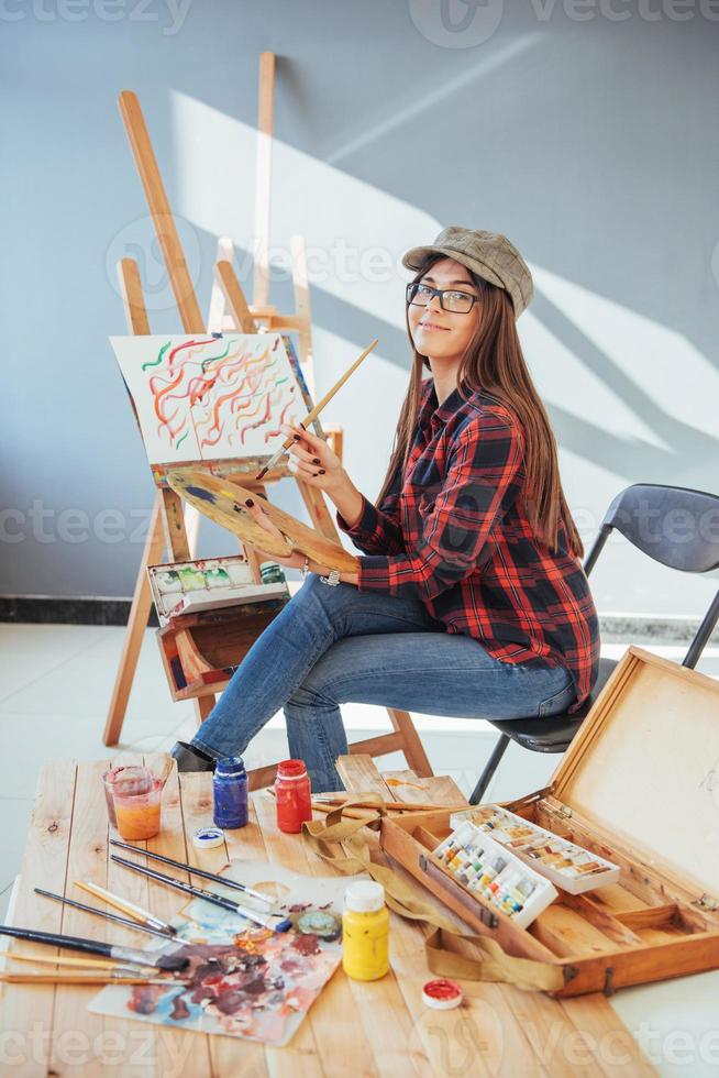 menina pintora pensativa criativa pinta um quadro colorido na tela com cores a óleo na oficina foto