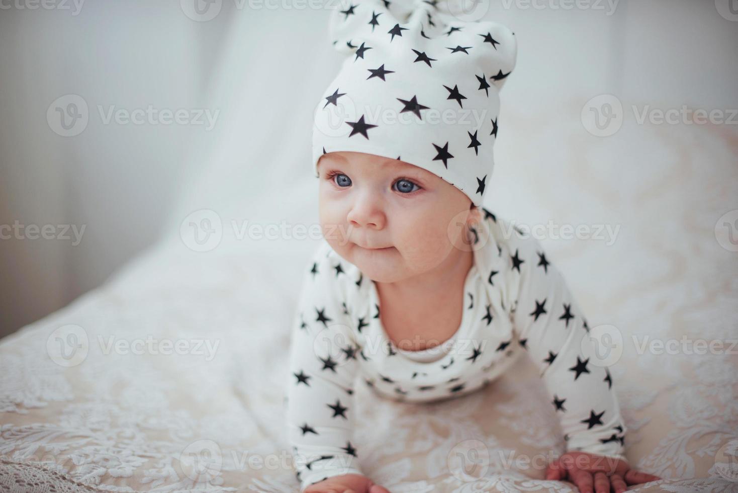 bebê recém-nascido vestido com um terno branco e estrelas negras é uma cama macia branca no estúdio foto