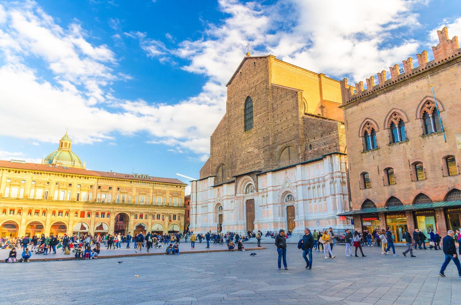 bolonha, itália, 17 de março de 2019 igreja basílica di san petronio e palácio palazzo dei banchi edifício na praça piazza maggiore e muitas pessoas andando no antigo centro histórico da cidade, emilia-romagna foto