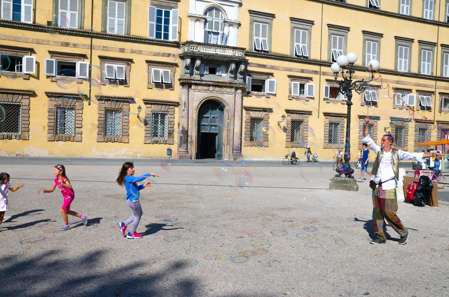 lucca, itália, 13 de setembro de 2018 homem está soprando bolhas de sabão coloridas e brincando com crianças pequenas foto