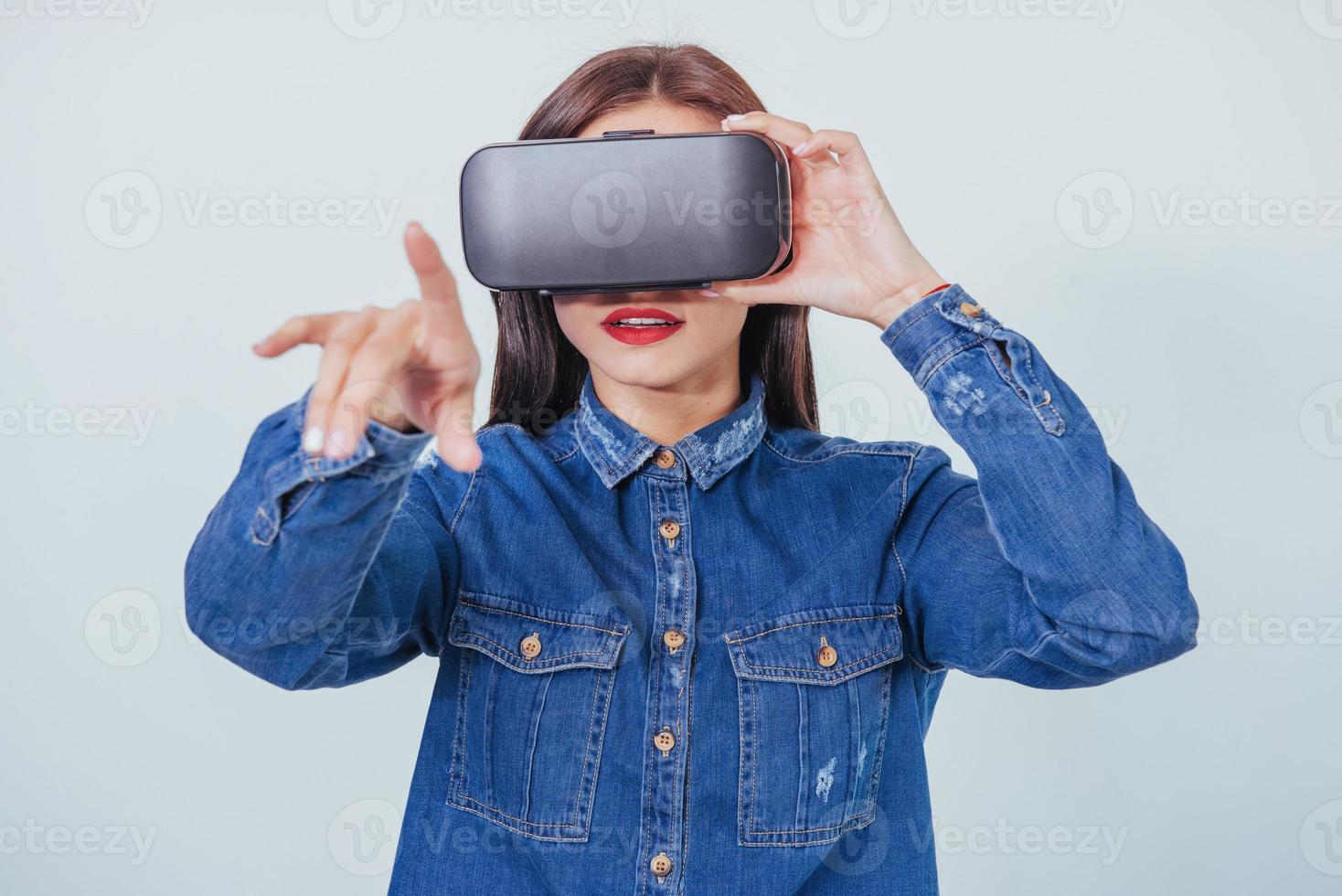 mulher bonita morena posando no estúdio, vestindo jeans, usando fones de ouvido de realidade virtual de óculos vr foto