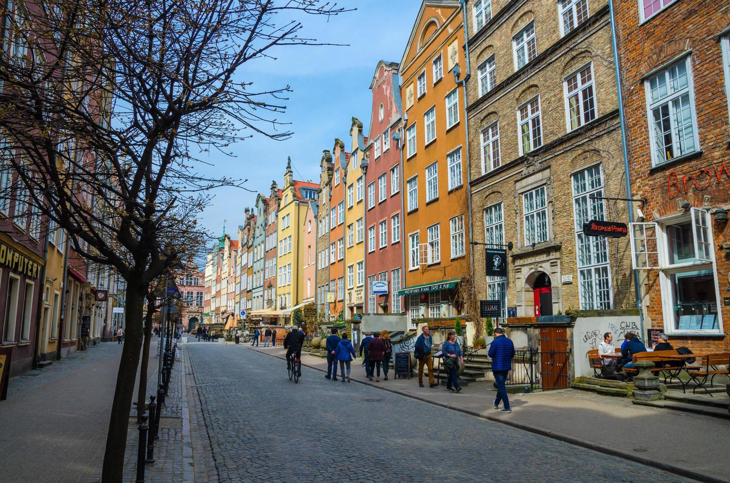 gdansk, polônia, 15 de abril de 2018 pessoas caminham ao longo do pavimento da rua piwna no antigo centro histórico da cidade com fachada de belas casas coloridas típicas, edifícios e árvores foto