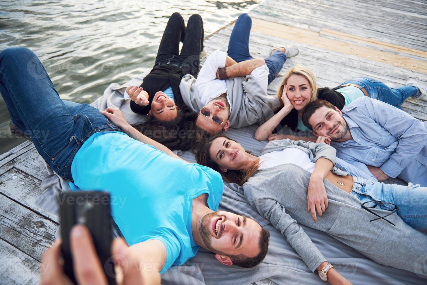 grupo de jovens bonitos que fazem selfies deitados no cais, os melhores amigos de meninas e meninos com conceito de prazer criam vida emocional das pessoas. foto