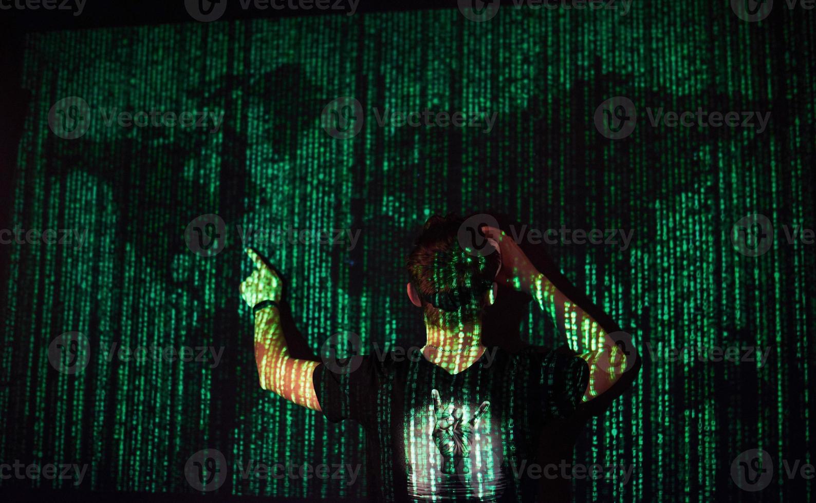 a dupla exposição de um homem caucasiano e fone de ouvido de realidade virtual é presumivelmente um jogador ou um hacker quebrando o código em uma rede ou servidor seguro, com linhas de código foto