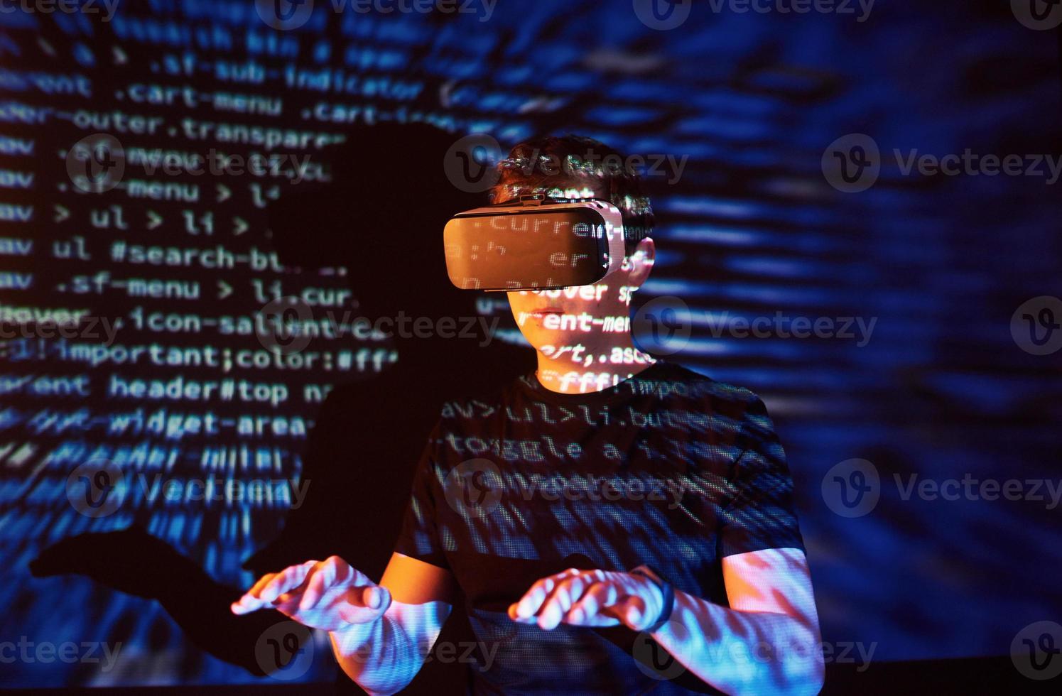 a dupla exposição de um homem caucasiano e fone de ouvido de realidade virtual é presumivelmente um jogador ou um hacker quebrando o código em uma rede ou servidor seguro, com linhas de código foto