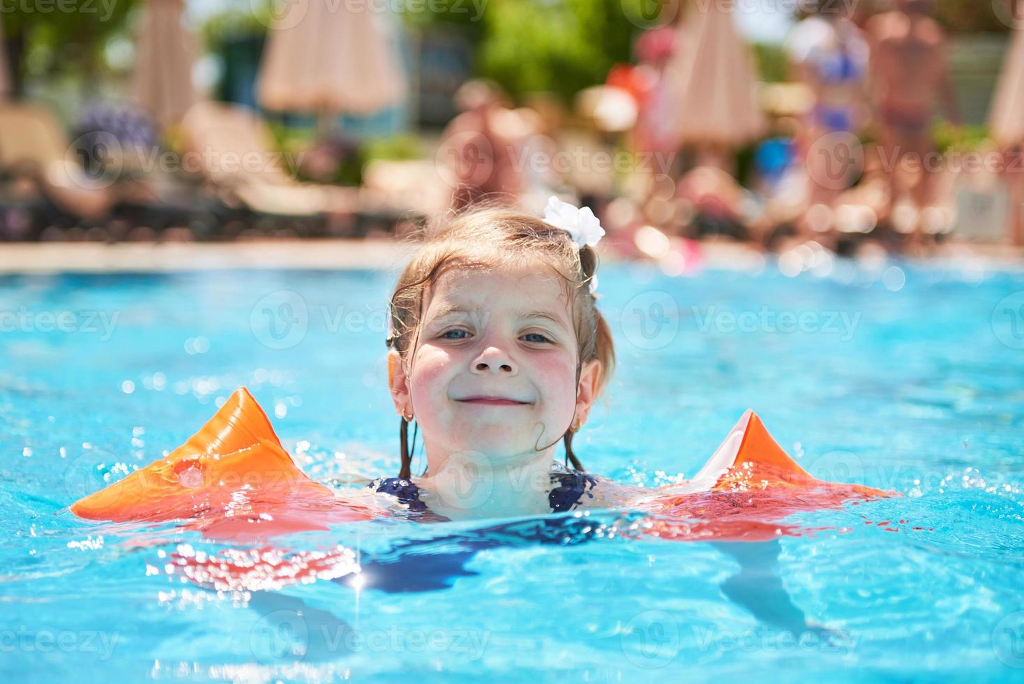 garota nadando na piscina em braceletes em um dia quente de verão. foto