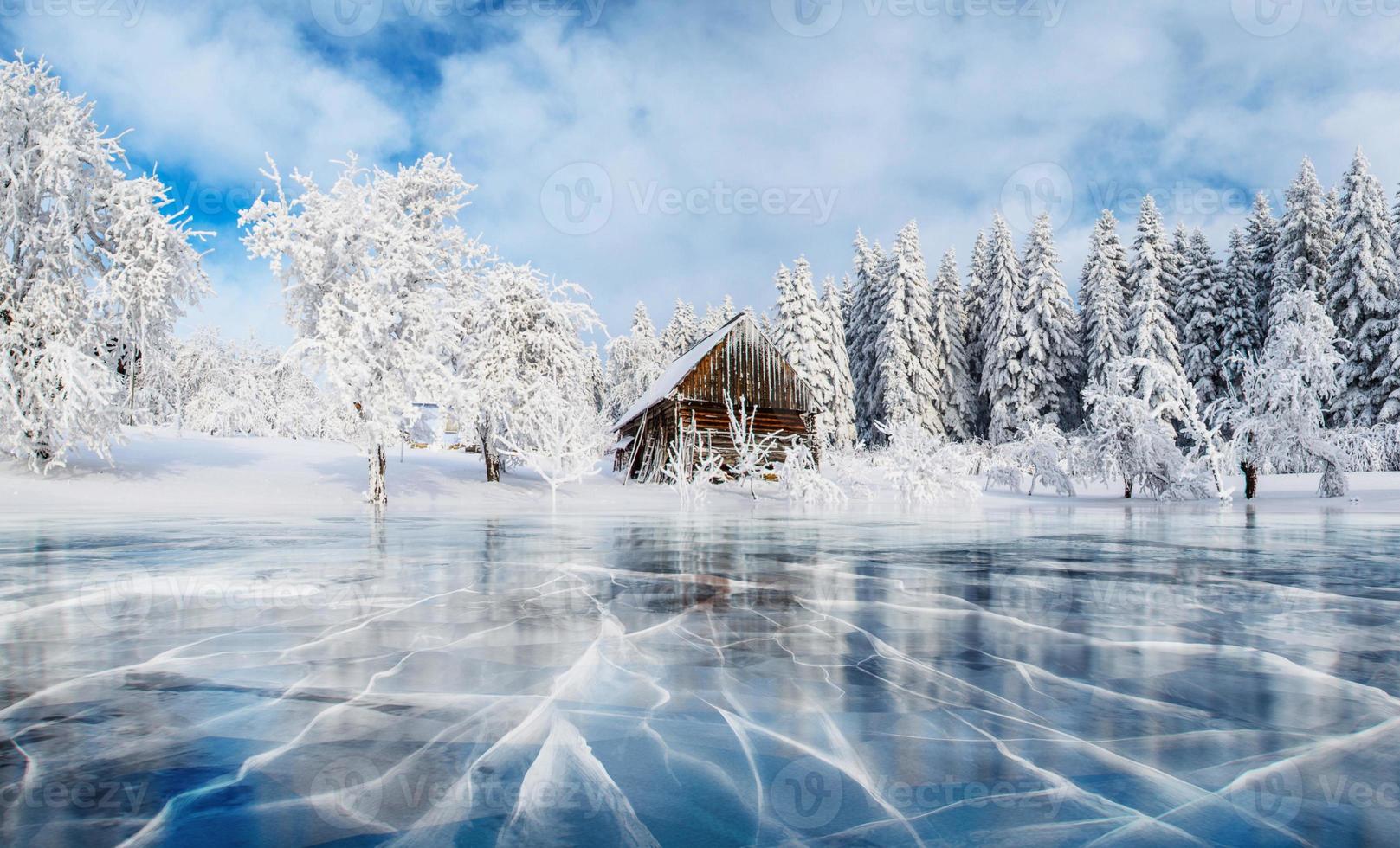 gelo azul e rachaduras na superfície do gelo. lago congelado sob um céu azul no inverno. cabana nas montanhas. névoa misteriosa. Cárpatos. Ucrânia, Europa foto