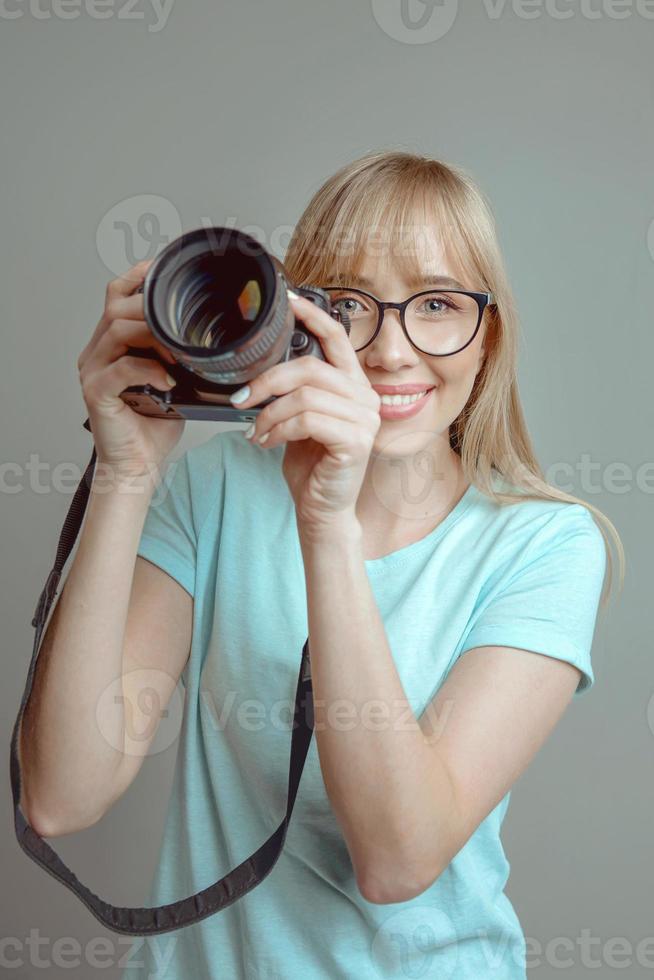 fotógrafo de mulher alegre elegante loira de óculos e segurando a câmera fotográfica. hobby, trabalho, conceito de tiro foto