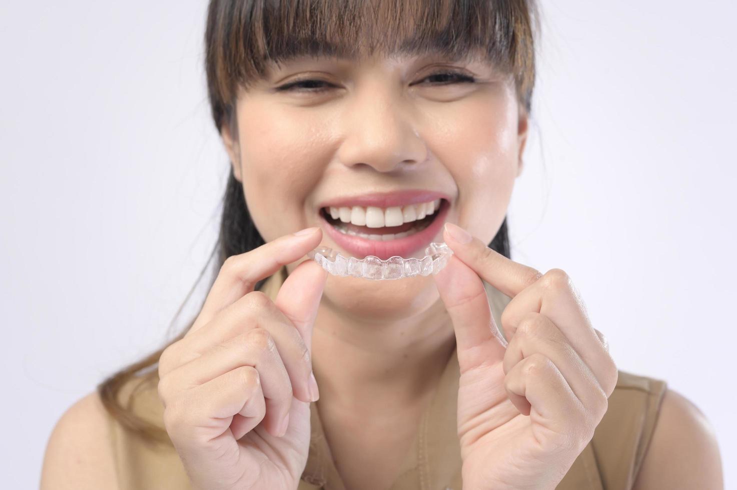 jovem mulher sorridente segurando aparelho invisalign sobre estúdio de fundo branco, saúde bucal e conceito ortodôntico. foto