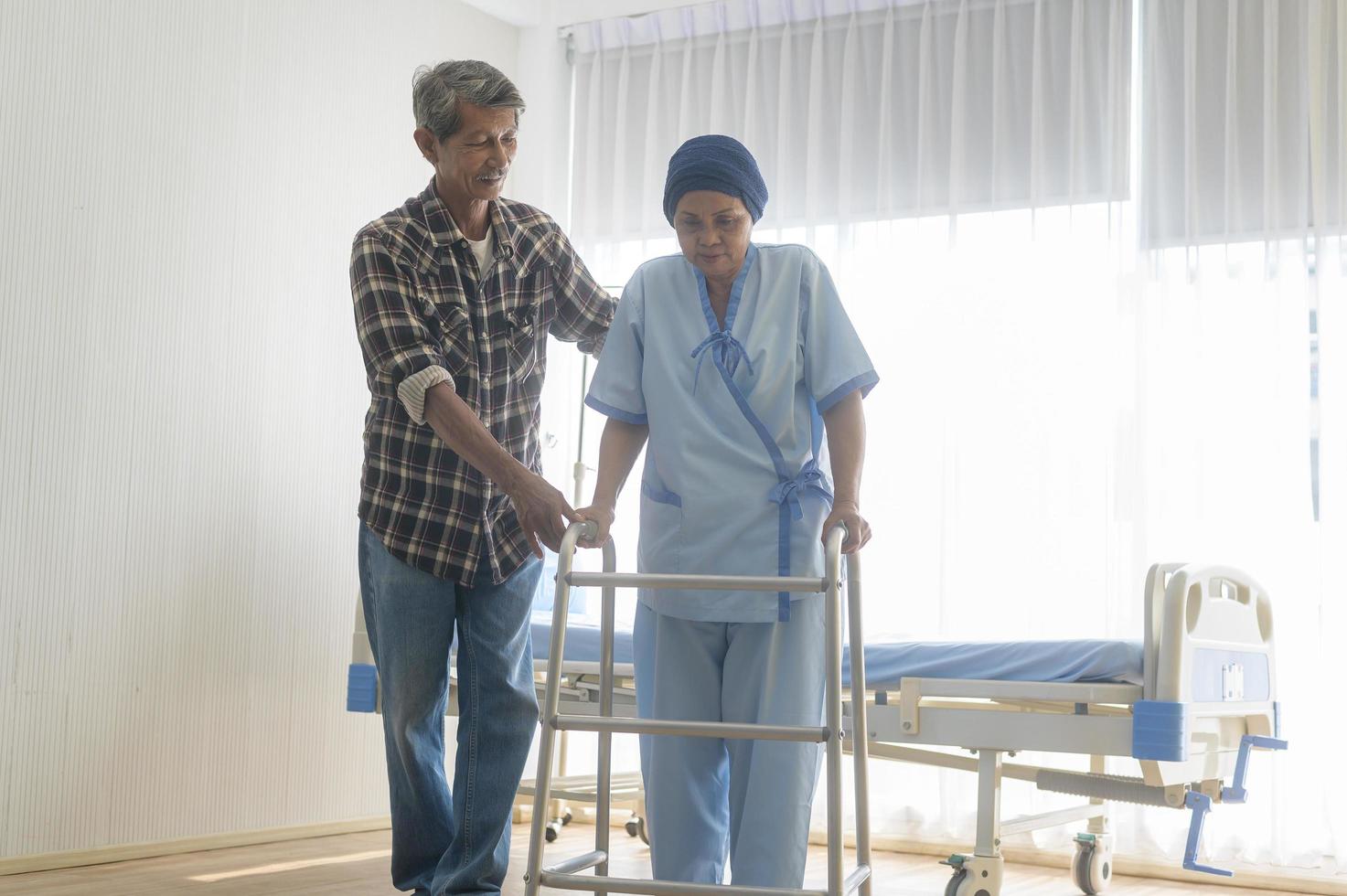 homem sênior ajudando mulher paciente com câncer usando lenço na cabeça com andador no hospital, cuidados de saúde e conceito médico foto