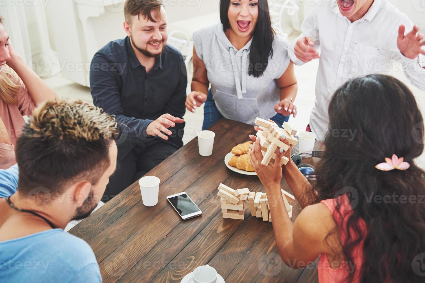 grupo de amigos criativos sentados à mesa de madeira. pessoas se divertindo jogando jogo de tabuleiro foto