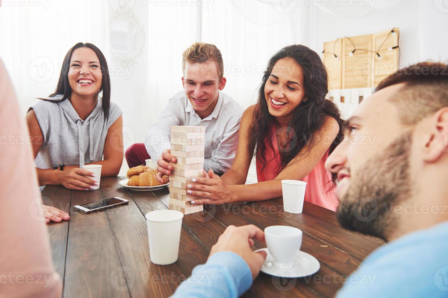 grupo de amigos criativos sentados à mesa de madeira. pessoas se divertindo jogando jogo de tabuleiro foto