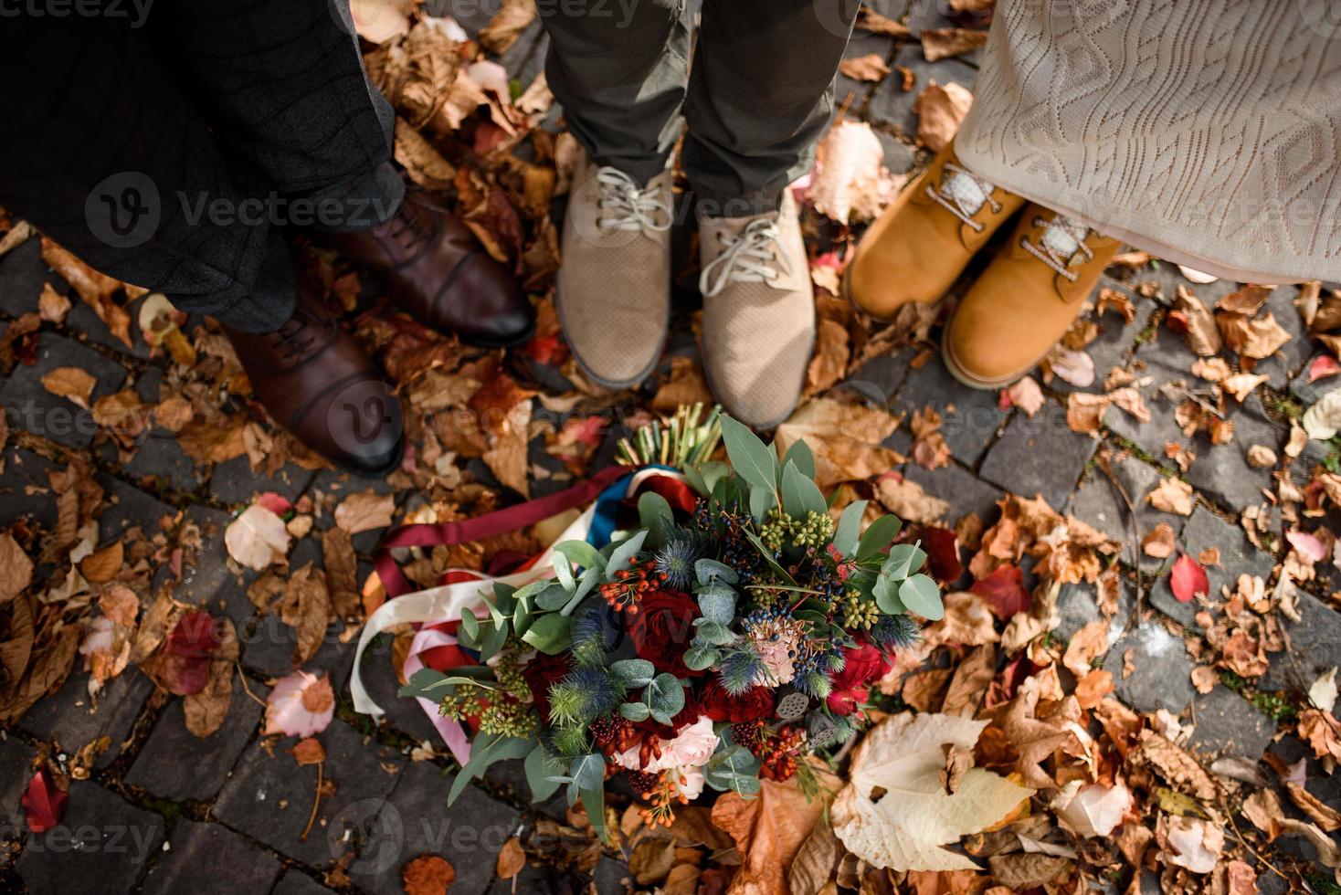 pés da noiva e do noivo, bem como seu filho no fundo das folhas de outono foto
