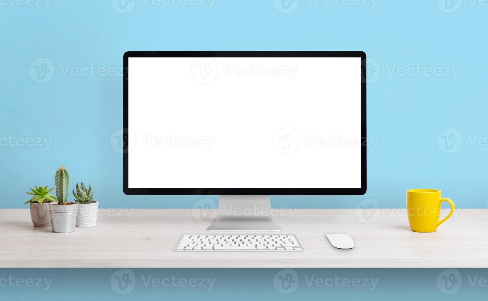 monitor de computador com tela branca isolada para apresentação na mesa de trabalho. composição limpa com caneca de café e plantas. parede azul no fundo foto