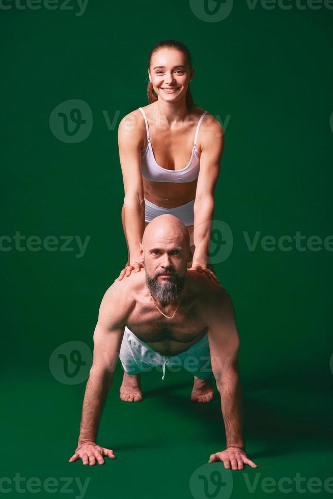 bela mulher desportiva e homem em roupas brancas fazendo asanas de ioga juntos interior em fundo verde foto