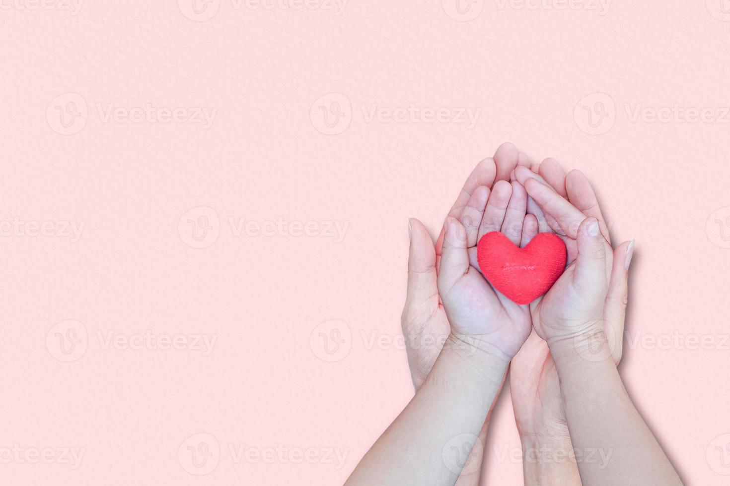 mão de adulto e criança segurando um coração vermelho sobre fundo rosa. vista superior, com espaço de cópia. conceitos de dia dos namorados. foto