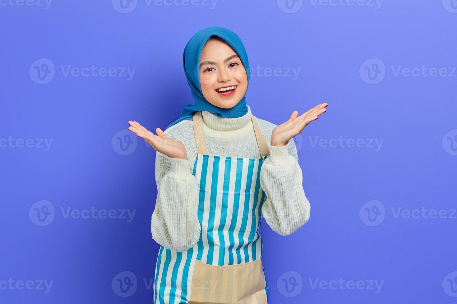 alegre jovem muçulmana asiática vestindo hijab e avental, comemorando o sucesso e recebendo boas notícias isoladas no fundo roxo. conceito de estilo de vida muçulmano dona de casa de pessoas foto