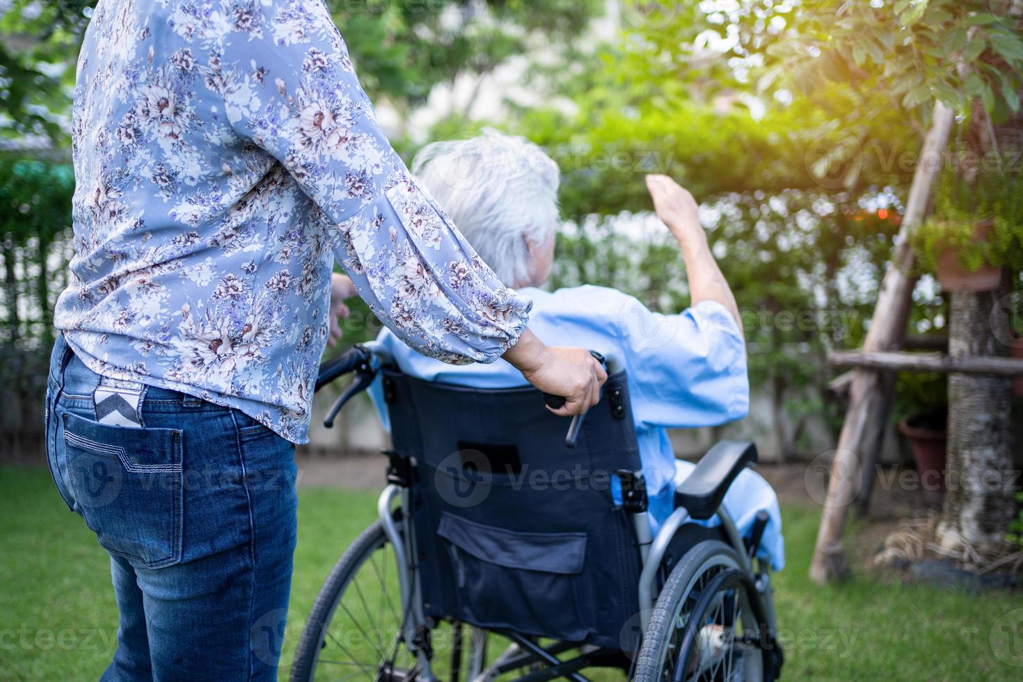 cuidador ajuda e cuida paciente idosa asiática ou idosa sentada na cadeira de rodas no parque na enfermaria do hospital de enfermagem, conceito médico forte e saudável. foto