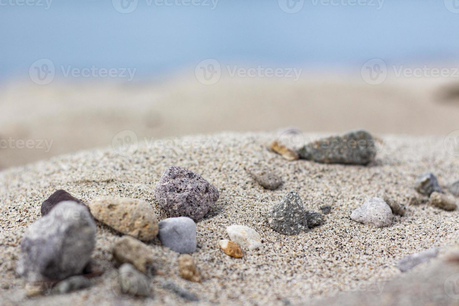 montanha de areia na praia cheia de pedras, mar embaçado e fundo de areia. uma pilha de areia de praia agradável com e pedras foto