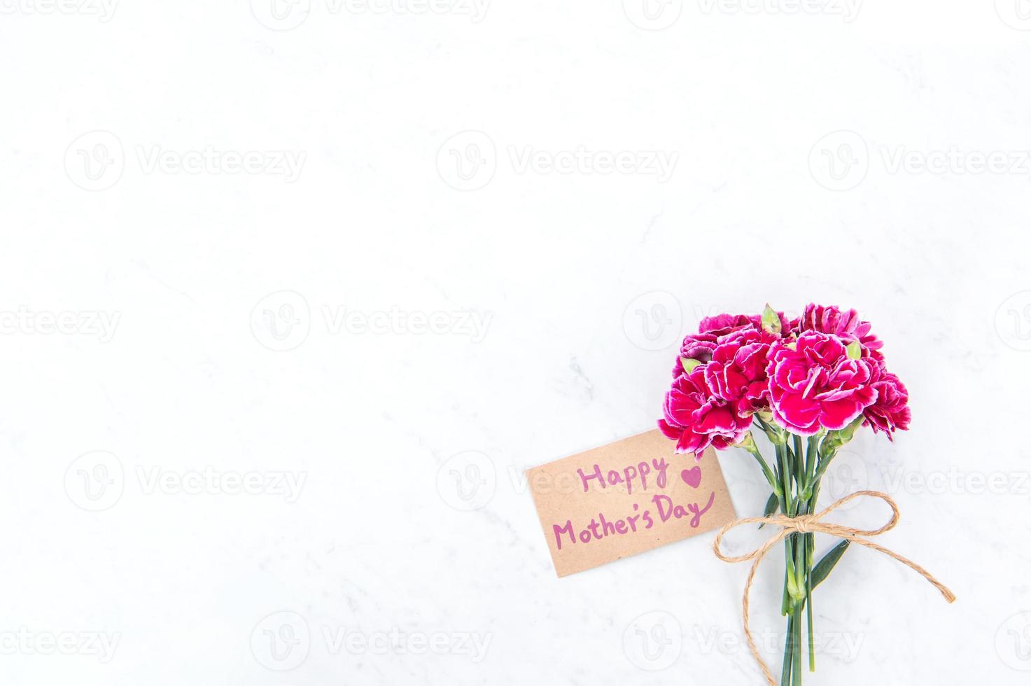 fotografia de conceito de ideia de dia das mães - belos cravos florescendo amarrados por arco com cartão de texto kraft isolado na mesa moderna brilhante, espaço de cópia, configuração plana, vista superior, mock up foto