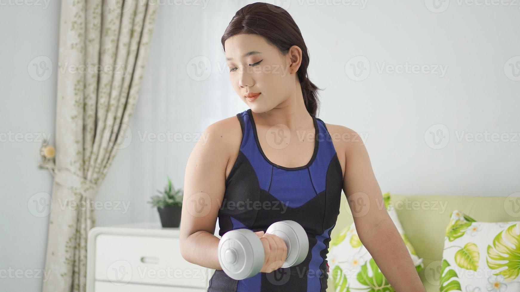 mulher asiática levantando barra de meio braço enquanto se agacha em casa foto