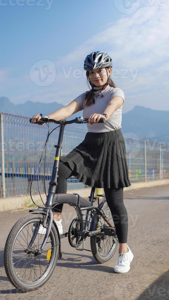 jovem mulher asiática gostando de andar de bicicleta quando parou na manhã de verão foto