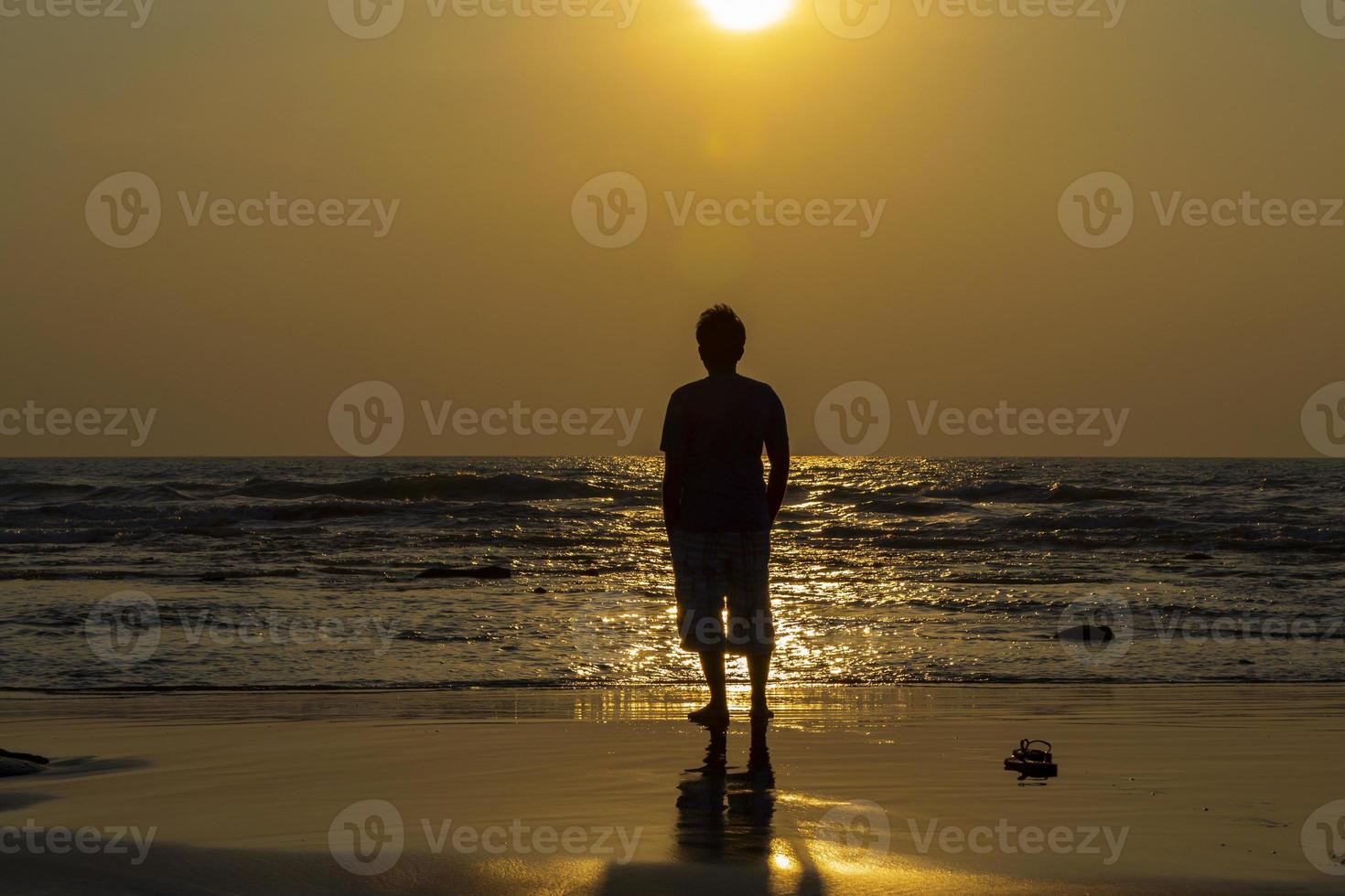 pôr do sol dourado à beira-mar com uma silhueta humana de frente para o sol foto