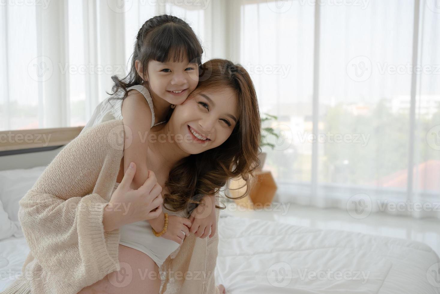mulher grávida asiática sentada na cama com a filha foto