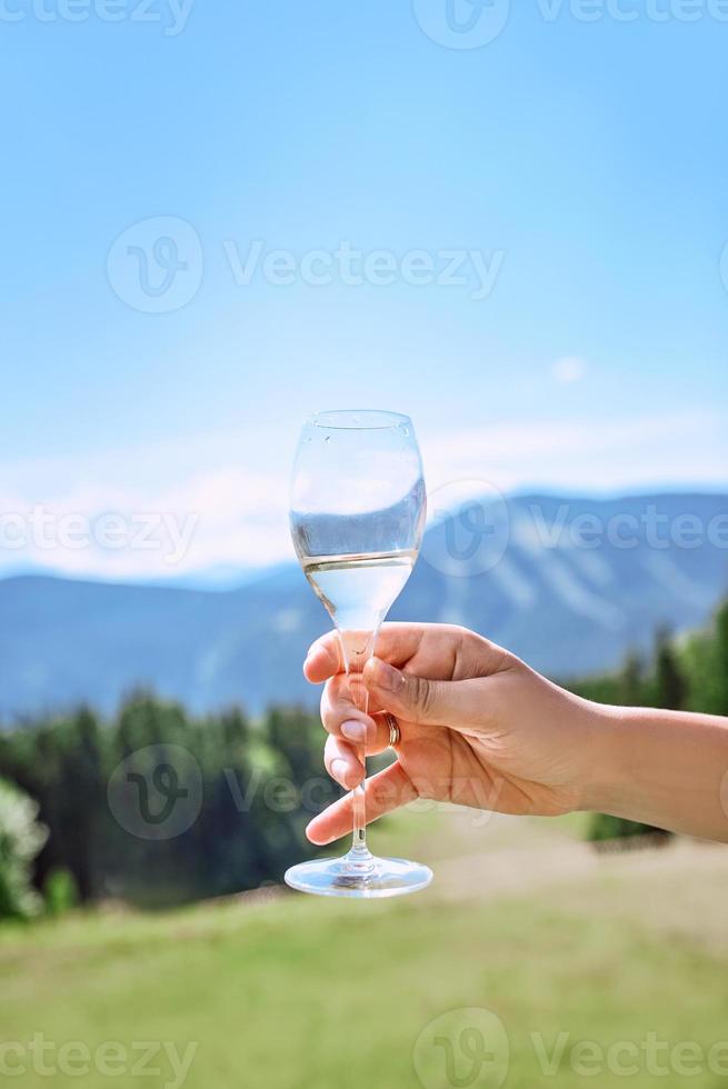 mão com copo de vinho espumante no fundo das montanhas foto