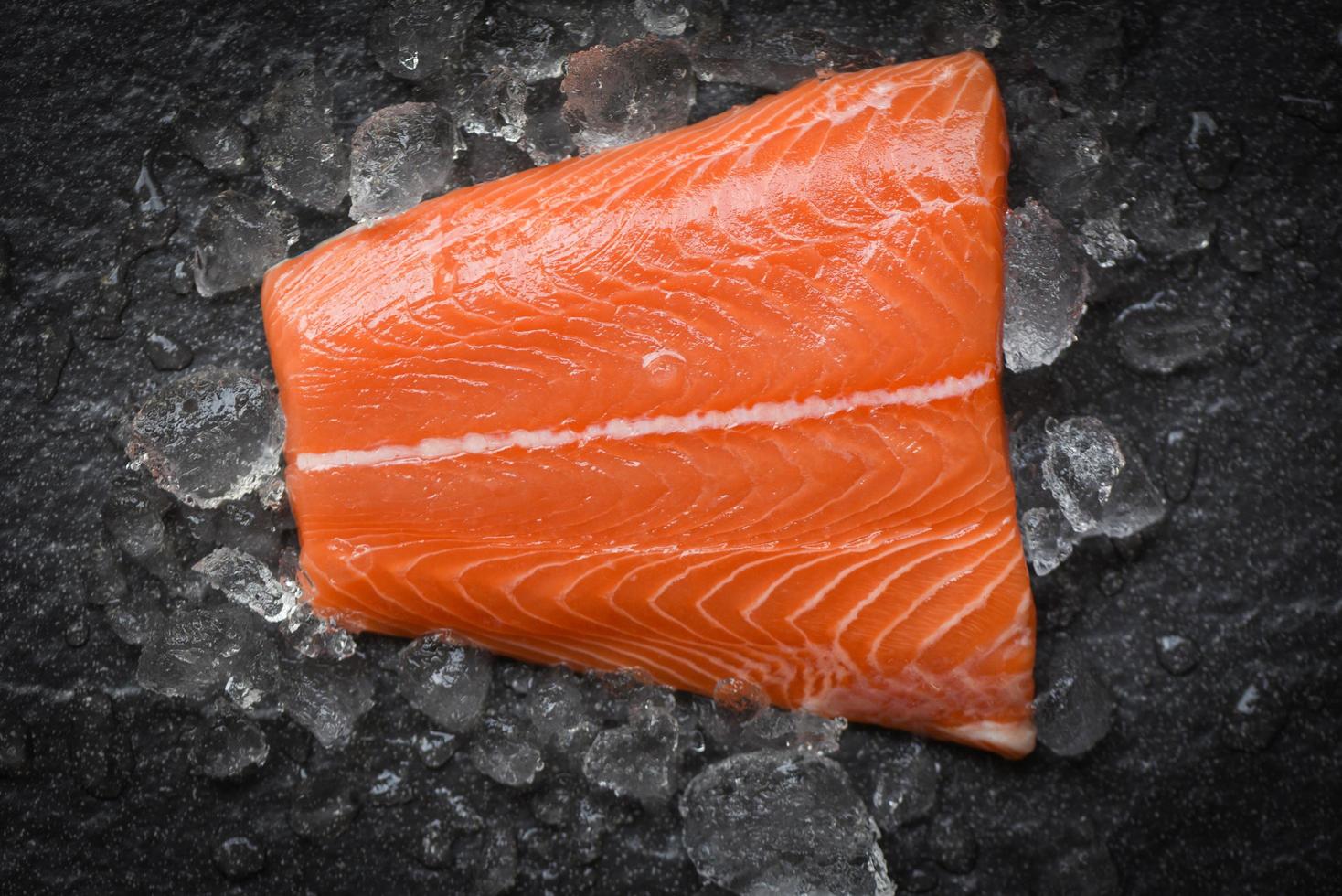 bife de peixe salmão cru fresco no gelo e fundo de pedra escura foto