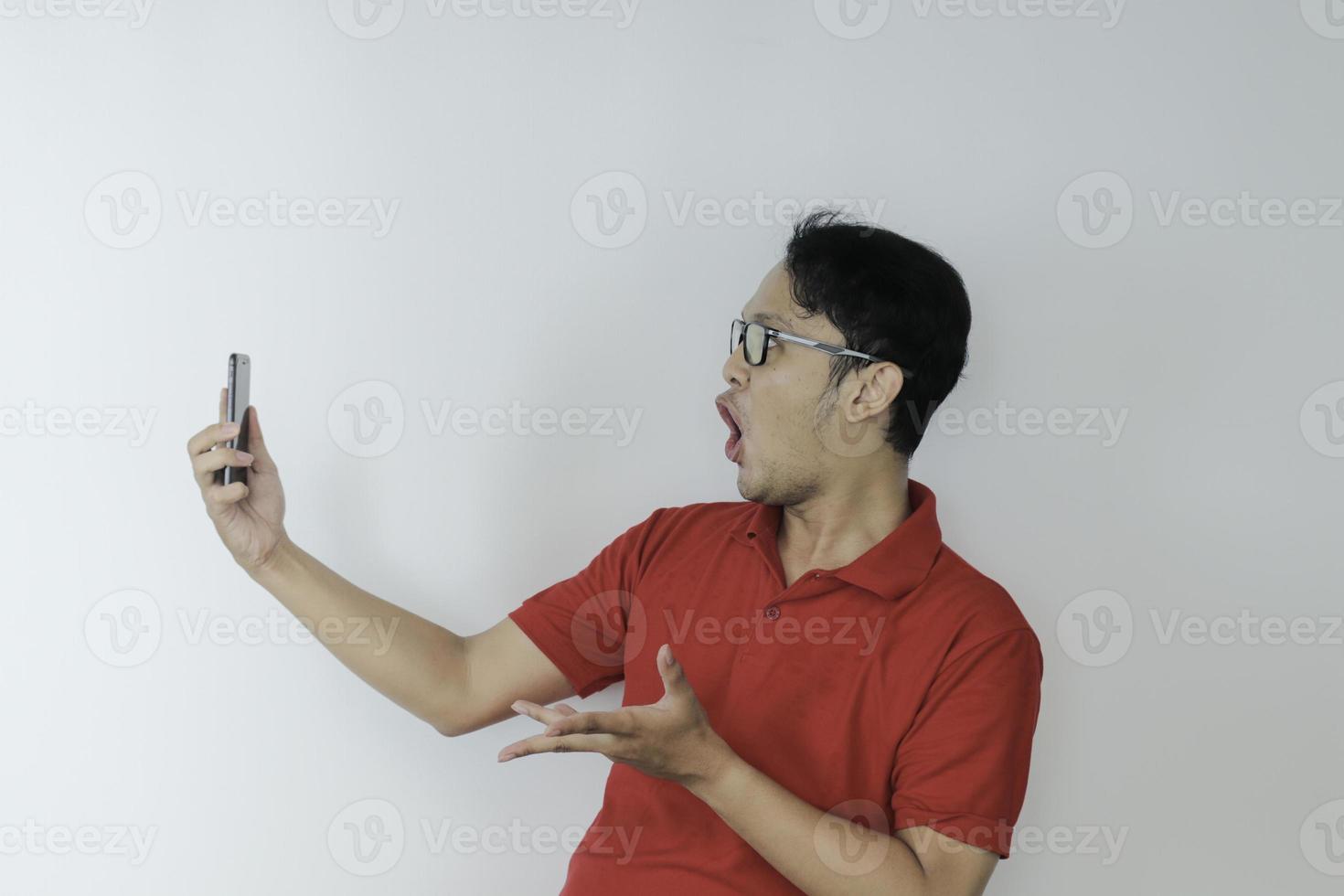 uau cara de jovem asiático chocou o que vê no smartphone em fundo cinza isolado. foto