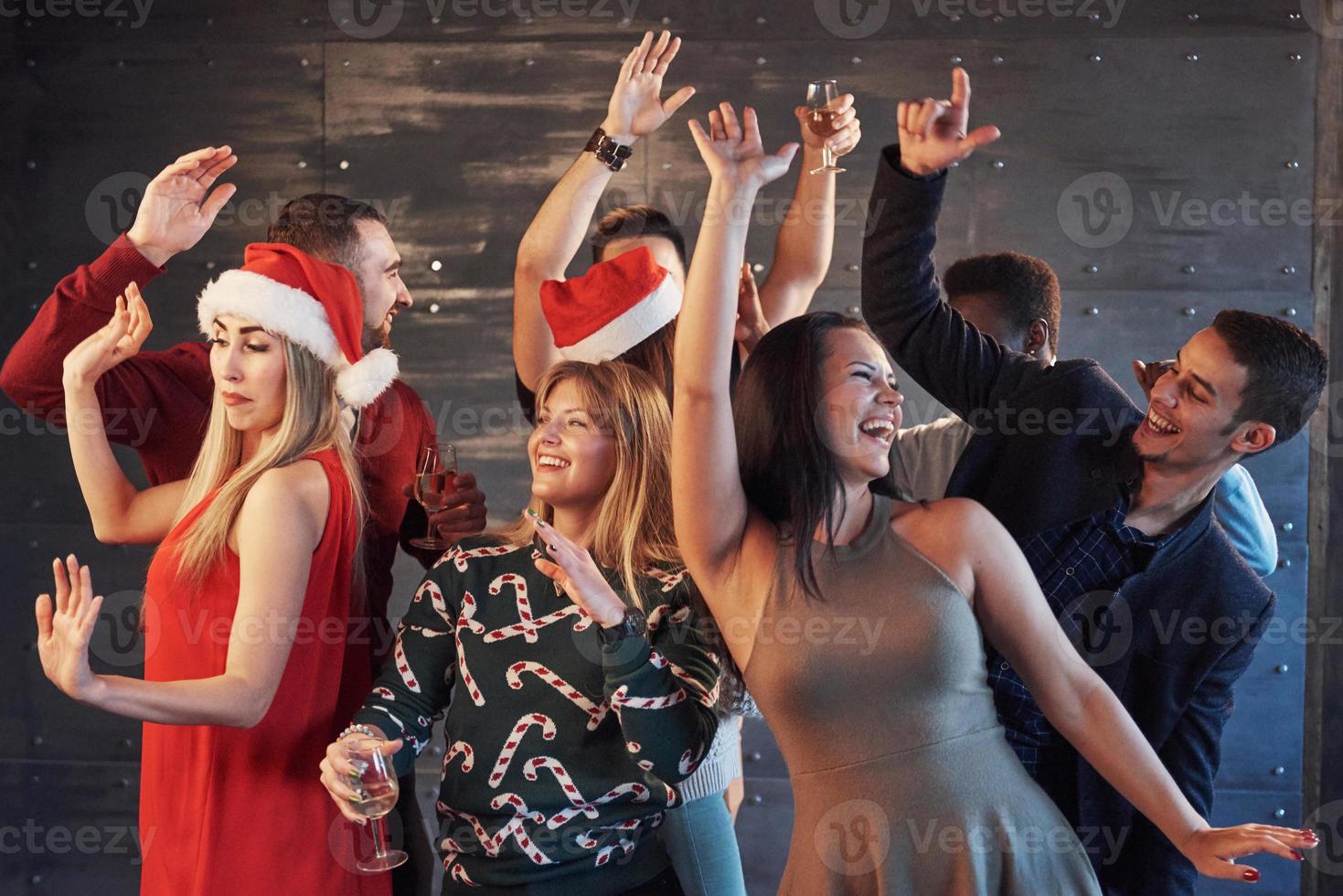 festa com amigos. eles amam o natal. grupo de jovens alegres carregando estrelinhas e taças de champanhe, dançando na festa de ano novo e parecendo feliz. conceitos sobre estilo de vida de união foto