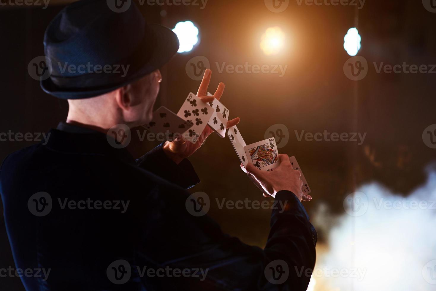 mágico mostrando truque com cartas de baralho. magia ou destreza, circo, jogo. prestidigitador em quarto escuro com neblina foto