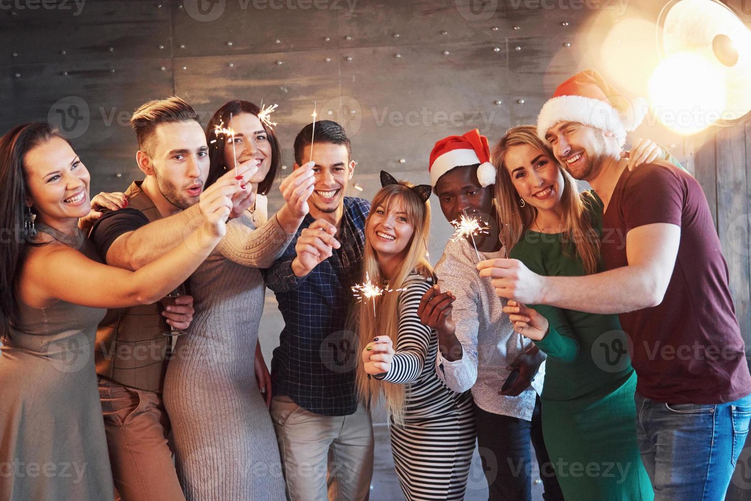 festa com amigos. grupo de jovens alegres carregando estrelinhas e taças de champanhe foto