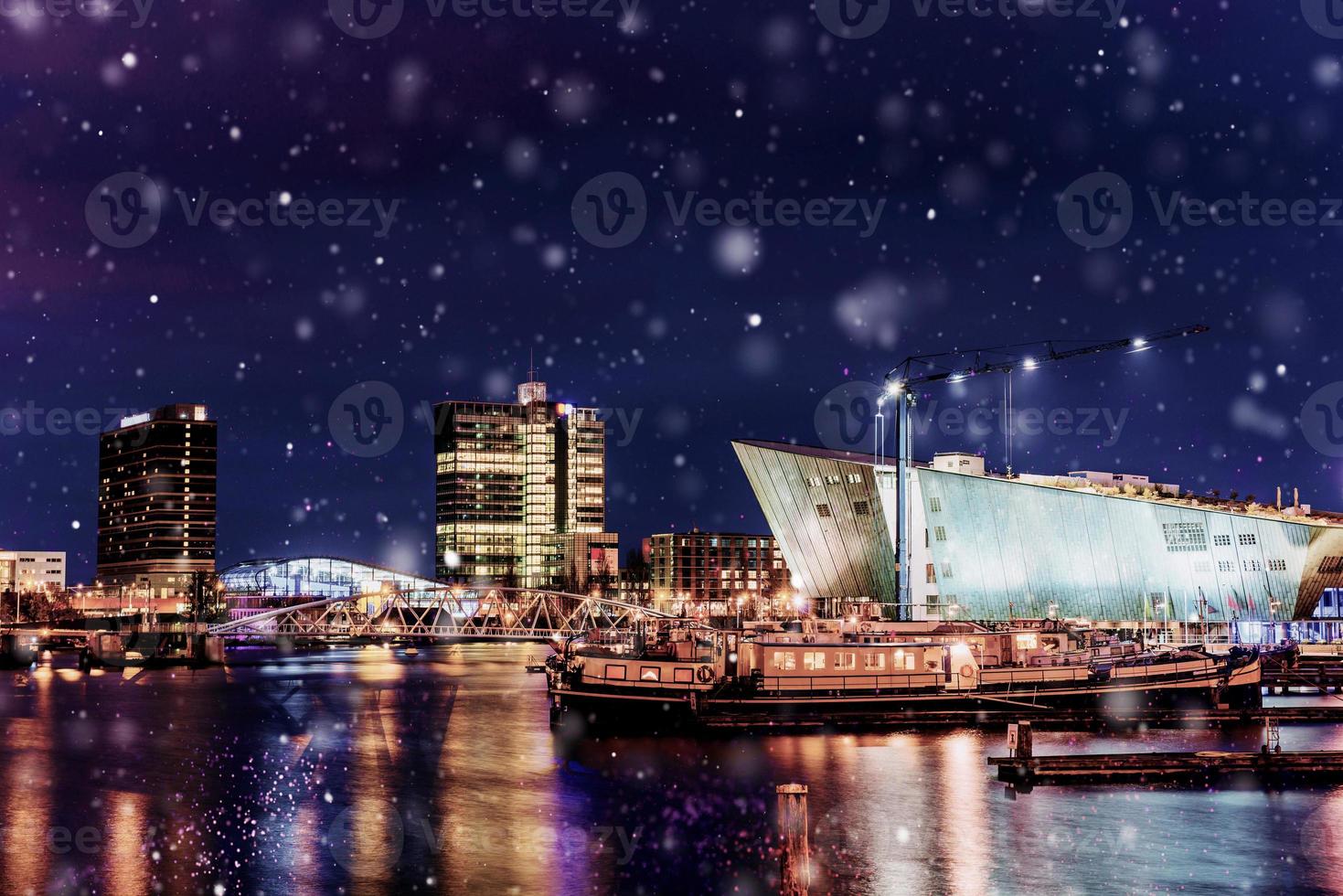 bela noite em amsterdã. iluminação noturna de edifícios e barcos perto da água no canal durante uma tempestade de neve. efeito de luz bokeh, filtro suave foto